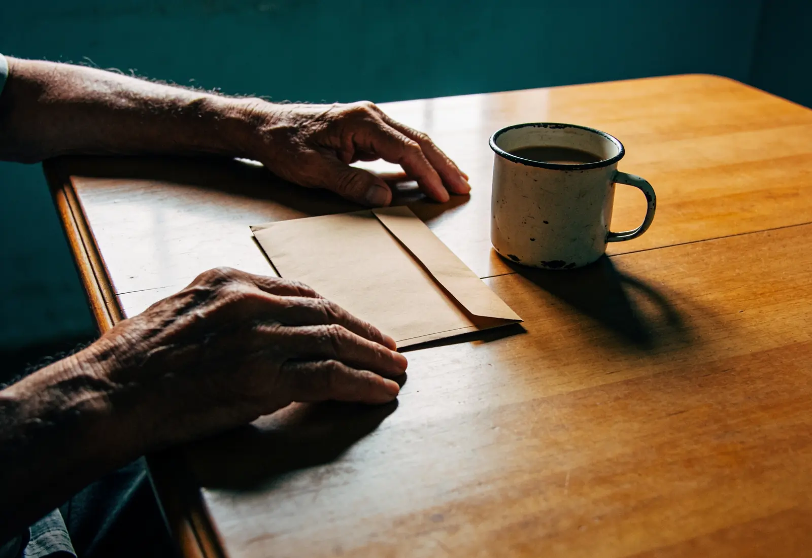 Mãos de um homem idoso sobre uma mesa de madeira, ao lado de uma calculadora de teclas grandes