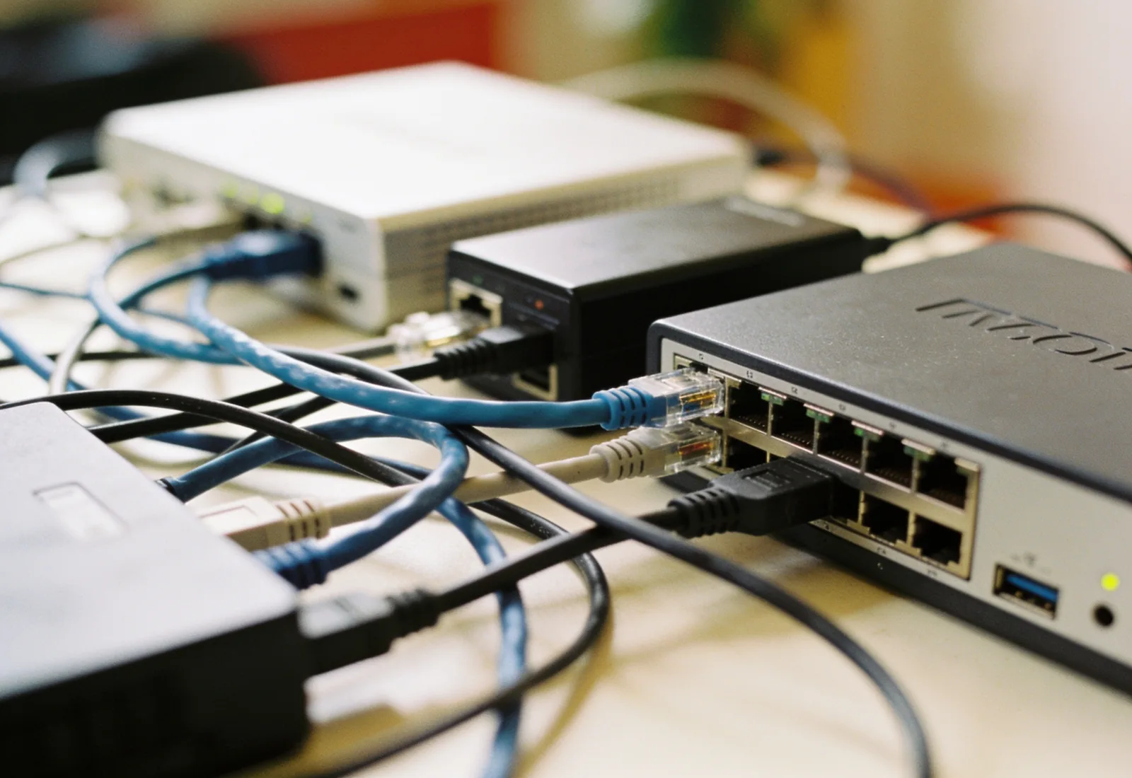Cabos de rede emaranhados e adaptadores ligando três aparelhos sobre uma mesa