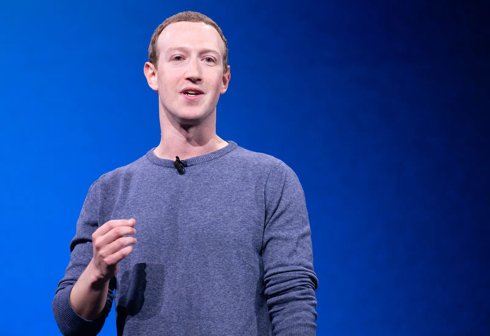 Mark Zuckerberg de pé no palco da conferência F8 de 2019, com o público sentado à frente e um telão azul ao fundo